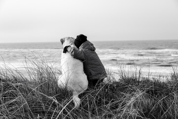 A girl and her dog are sitting on the beach, looking out to sea and enjoying the peace and beauty of nature.