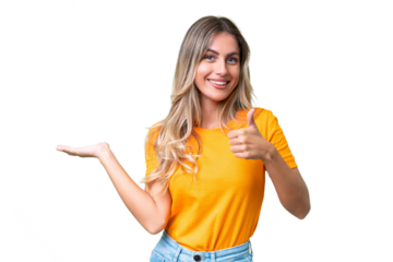Young Uruguayan woman over isolated background holding copyspace imaginary on the palm to insert an ad and with thumbs up