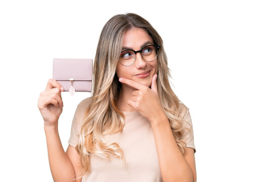Young Uruguayan woman holding a wallet over isolated background thinking an idea and looking side