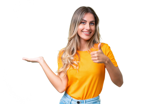 Young Uruguayan woman over isolated background holding copyspace imaginary on the palm to insert an ad and with thumbs up