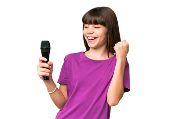 Little singer girl picking up a microphone over isolated background celebrating a victory