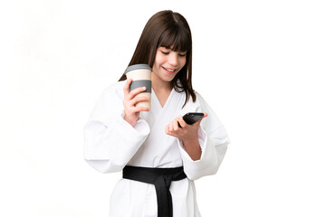 Little Caucasian girl doing karate over isolated background holding coffee to take away and a mobile