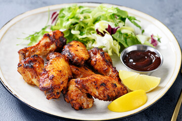 Air fryer chicken wings with fresh green salad, barbecue sauce and lemon slices.