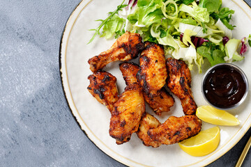 Air fryer chicken wings with fresh green salad, barbecue sauce and lemon slices. top view