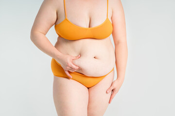 Tummy tuck, flabby skin on a fat belly, plastic surgery concept on gray background - 745106283