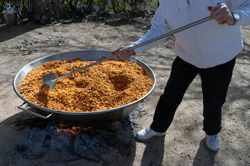Un cocinero prepara al aire libre una gran sartén de migas castellanas en una comida popular.