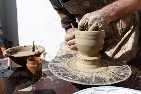 Un alfarero trabajando en el torno sobre una vasija de arcilla con sus manos.