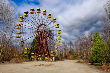 An idle Ferris wheel with yellow cars in a desolate area.