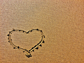 A heart is etched into a sandy surface, showing a clear contrast.