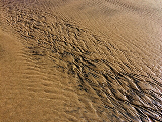 The image captures a close-up of sand with intricate patterns formed by the flow of water.