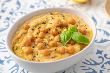 A bowl of hummus with chickpeas and basil on a table
