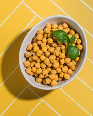 a bowl of chickpeas with basil leaves on a yellow table