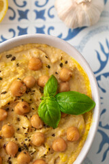 A bowl of hummus with chickpeas and basil on a table