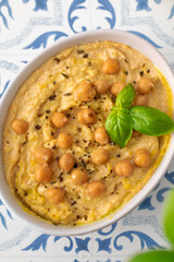 A bowl of hummus with chickpeas and basil on a table