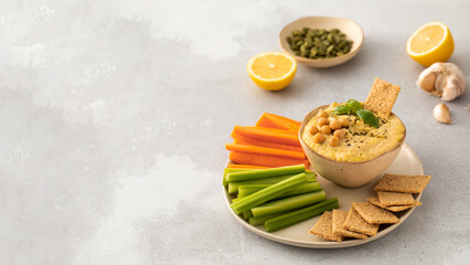 A dish of hummus with a side of carrots, celery and more hummus on a plate. Copy space