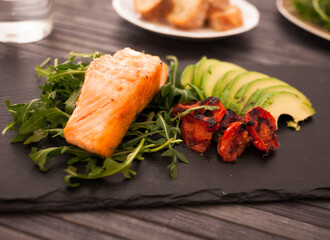 Baked sea trout fillet with fresh vegetables and herbs on black board