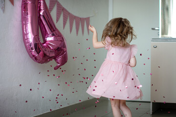 Indoors, on her birthday, a girl in a pink dress spins in confetti falling from above against the...
