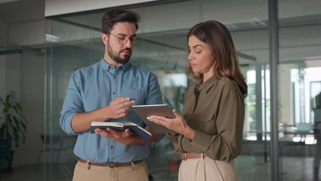 Happy busy latin partners using digital tablet talking in office. Professional business people having conversation using tab at meeting. Female executive manager working together with male employee.
