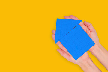 Blue Puzzle House Held in Both Hands on Yellow Background