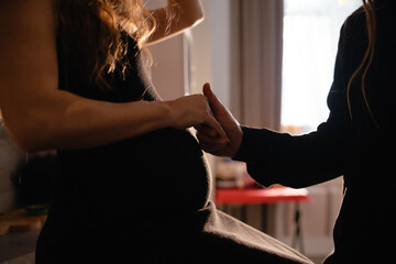 The pregnant woman sitting next to a man is gently holding her belly with one hand while the other rests on his thigh, showing a gesture of comfort and sharing a special moment