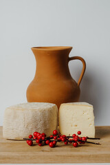 Two pieces of cheese and a pitcher of milk are placed on a wooden cutting board, surrounded by drinkware and tableware