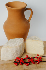 An assortment of tableware including a clay pitcher, a piece of cheese, and red berries displayed on a wooden table. Perfect for a creative artsthemed gathering