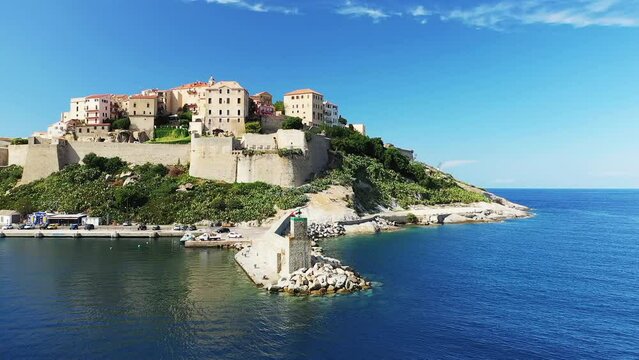 The lighthouse at the entrance to the port of the city of Calvi and its medieval fort , in Europe, France, Corsica, by the Mediterranean Sea, in summer, on a sunny day.