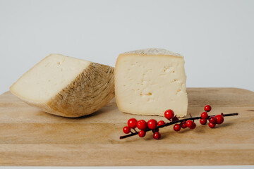 A piece of cheese is displayed on a wooden cutting board alongside red berries. This food pairing can be used as an ingredient in various recipes or enjoyed as a delicious snack