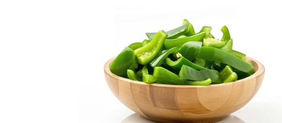A wooden bowl filled with freshly sliced green peppers sits isolated on a white background. The vibrant green peppers create a striking contrast against the rustic wooden bowl.