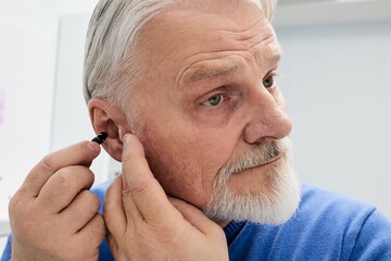 Grey-haired senior man with hearing impairment using hearing aid. Hearing solutions for deafness...