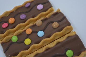 Sweets, delicious, interesting desserts, cookies with caramel, milk chocolate and small colored candies arranged on a white background.