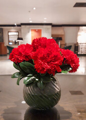A bunch of bright red hibiscus flowers in a green vase placed on a granite table.