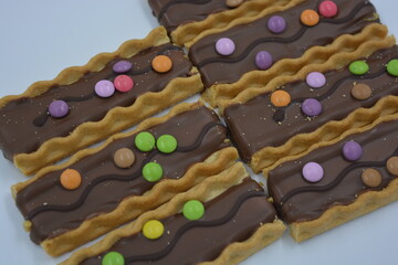 Sweets, delicious, interesting desserts, cookies with caramel, milk chocolate and small colored candies arranged on a white background.