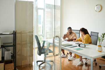 Coworkers sitting at table in meeting room discussing ideas for mobile app update
