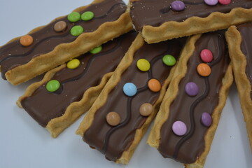 Sweets, delicious, interesting desserts, cookies with caramel, milk chocolate and small colored candies arranged on a white background.