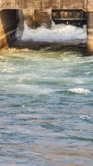 Bluewater gushed out of the barrage gate. White horses rush out of the dusty rugged brown concrete walls of a dam.