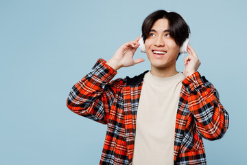 Young minded man of Asian ethnicity he wearing red hoody casual clothes listen to music in headphones look aside on area mockup isolated on plain pastel light blue cyan background. Lifestyle concept.