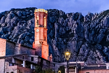 Views of the illuminated Church of Sant Corneli in Collbato, Barcelona at dusk, with the Montserrat mountain in the background