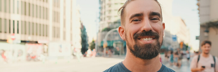 Close-up of young smiling man with beard standing in front of busy intersection, Panorama