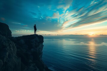 A person stands on a cliff overlooking the ocean at sunset.