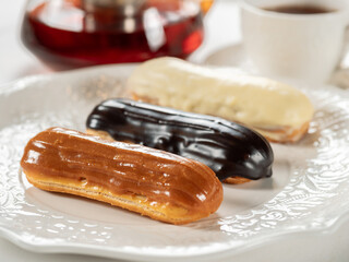 Group of french dessert Eclair on white plate. Caramel, chocolate and vanilla glazed eclairs on...