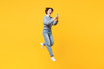 Fototapeta na wymiar Full body excited young woman she wears grey knitted sweater shirt casual clothes jump high hold in hand use mobile cell phone isolated on plain yellow background studio portrait. Lifestyle concept.