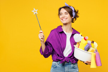 Young smiling woman wear purple shirt hold basin with detergent bottles do housework tidy up hold...