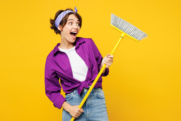 Young shocked excited happy fun woman she wear purple shirt casual clothes do housework tidy up hold in hand broom look aside isolated on plain yellow background studio portrait. Housekeeping concept - obrazy, fototapety, plakaty