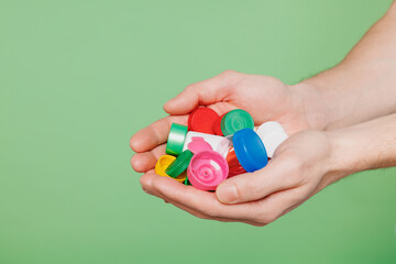 Close up cropped male volunteer holding in hand plastic bottle cups to recycle isolated on pastel...