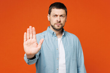 Young sad dissatisfied displeased man wear blue shirt white t-shirt casual clothes showing stop gesture with palm look camera isolated on plain red orange background studio portrait Lifestyle concept