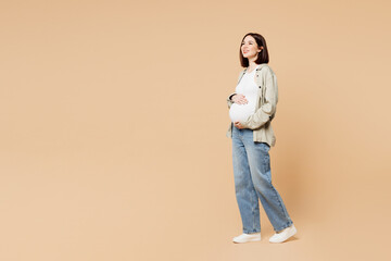 Plakaty  Full body side view young minded pregnant woman future mom in grey shirt with belly stomach stroking put hand on tummy with baby isolated on plain beige background Maternity family pregnancy concept