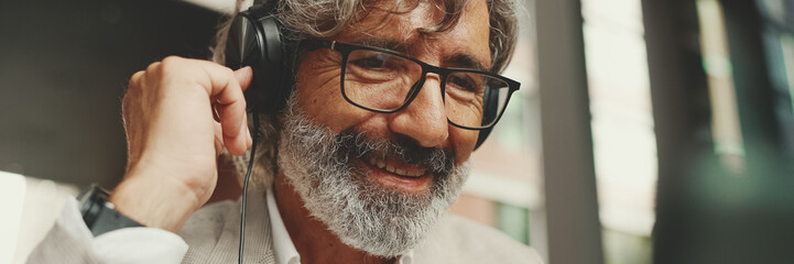 Panorama, Close up portrait of mature businessman with beard in eyeglasses and headphones, sits in...