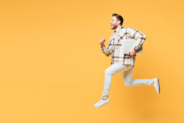 Fototapeta na wymiar Full body side view young smart fun IT man he wears brown shirt casual clothes jump high hold use work on laptop pc computer run isolated on plain yellow orange background studio. Lifestyle concept.