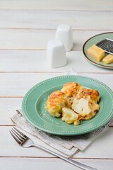 Cooked cauliflower grantin with bechamel sauce and cheese on a green ceramic plate on a light wooden background. Vegetarian recipes; side dishes.